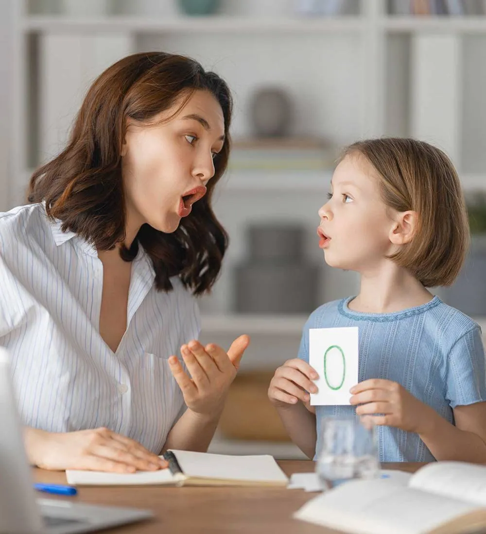 An adult supporting a child during a speech activity at a table